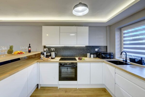 A modern kitchen with white cabinets, a wooden countertop, a built-in oven, and a window with blinds.
