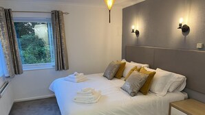A neatly made bed with white and gold pillows, a bedside table with drawers, and a window with curtains. - Tranquil Retreat on the Edge of the Countryside (Blaydon-on-Tyne)