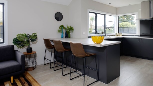 Una cocina moderna con una isla central, taburetes de bar y un amplio ventanal que proporciona luz natural.