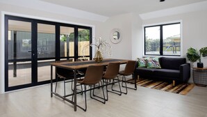 Una sala de estar moderna con una mesa de comedor, sillas, un sofá y un ventanal grande.