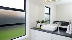Un baño moderno con un espejo grande, muebles blancos, un lavabo y una ventana con marco negro.