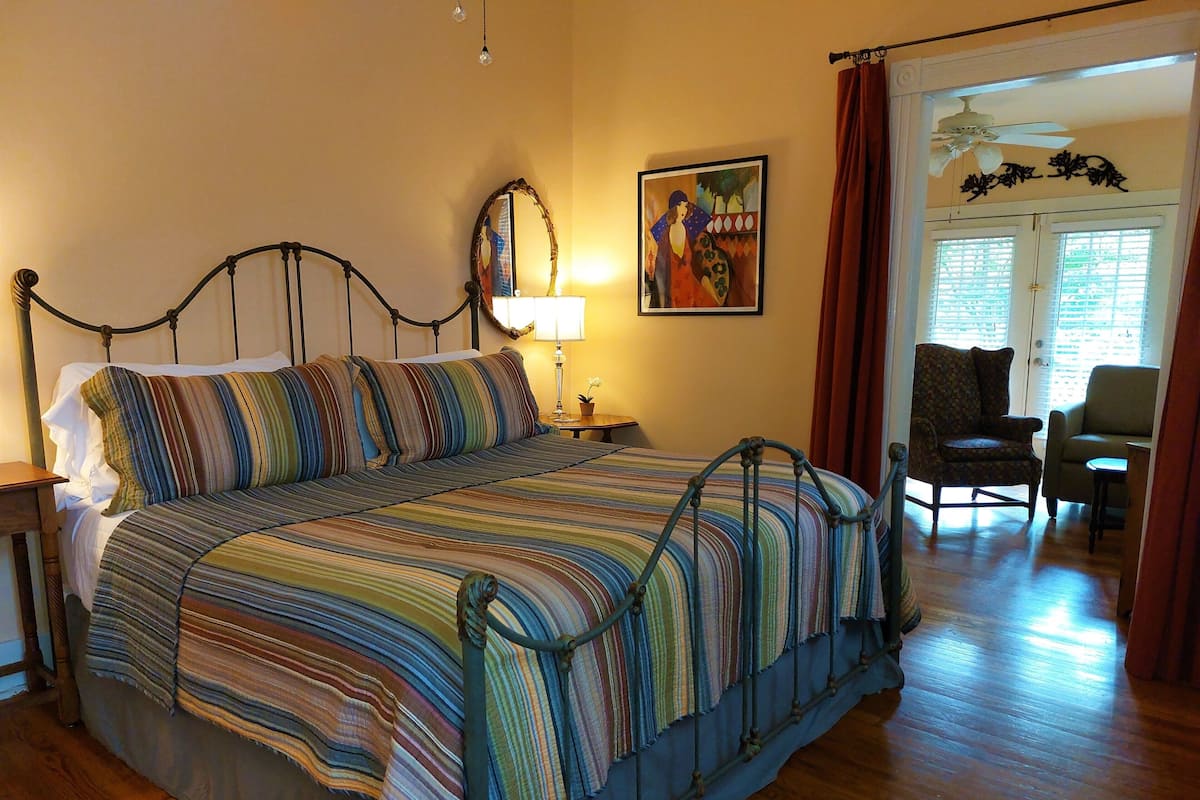 Un lit avec une couvre-lit à rayures, une table de chevet avec une lampe, une chaise et un tableau accroché au mur.