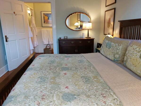 Un dormitorio con colcha estampada, cabecera de madera, cómoda con espejo y lámpara de noche.