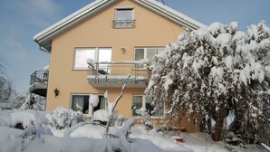 A two-story building with a balcony, snow-covered trees, and a clear sky.
