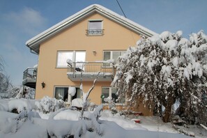 Un bâtiment à deux étages doté d’un balcon, des arbres couverts de neige et un ciel dégagé.