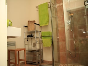 Une salle de bain avec une douche à parois de verre, un porte-serviettes en métal et un tabouret en bois.