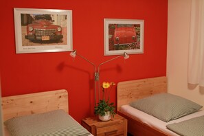 Une chambre avec deux lits, une table de chevet avec une lampe et deux tableaux encadrés au mur.