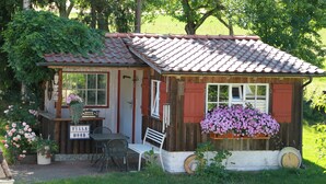 A small wooden building with a tiled roof, a bench, a table, and a sign that reads 'Villa Moor.'