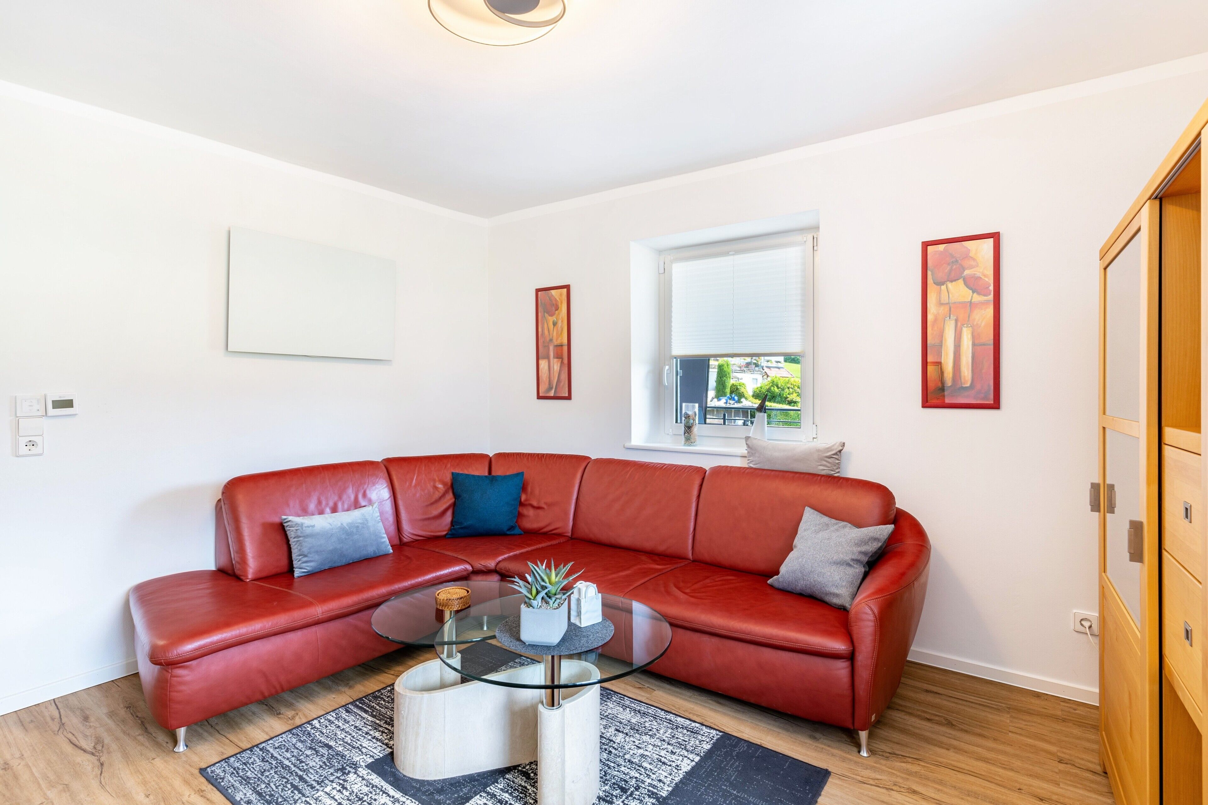 Un salon moderne avec un canapé en cuir rouge, une table basse en verre et une fenêtre équipée de stores.