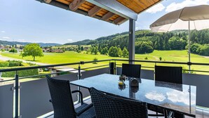 Ein Balkon mit Tisch und Stühlen, einer Holzbalkendecke und Blick auf eine grüne Landschaft.