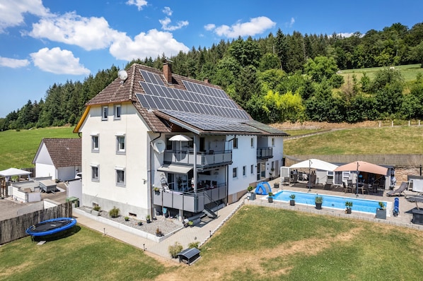 Una casa de dos pisos con paneles solares, piscina y un trampolín.