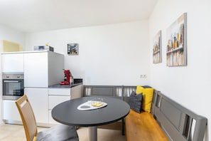 Una cocina moderna con zona de comedor, que incluye una mesa redonda con bandeja, un banco con cojines y un refrigerador.