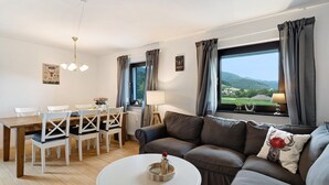 Una sala de estar moderna con comedor, un sofá con un cojín decorativo, una mesa de centro redonda y vistas al exterior.