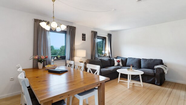 Una sala de estar moderna con una mesa de comedor de madera, sillas blancas, un sofá gris y una pequeña mesa de centro blanca.