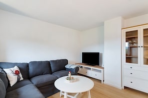 Ett modernt vardagsrum med en grå soffa, ett vitt soffbord, en platt-TV och ett träskåp.