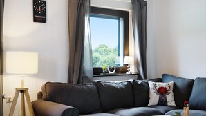 Una sala de estar moderna con un sofá, una lámpara, un reloj y una ventana con cortinas.