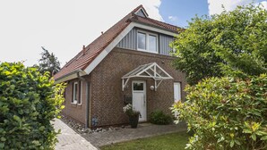 Ett hus byggt av tegel med ett sluttande tak, en liten veranda och en trädgård.