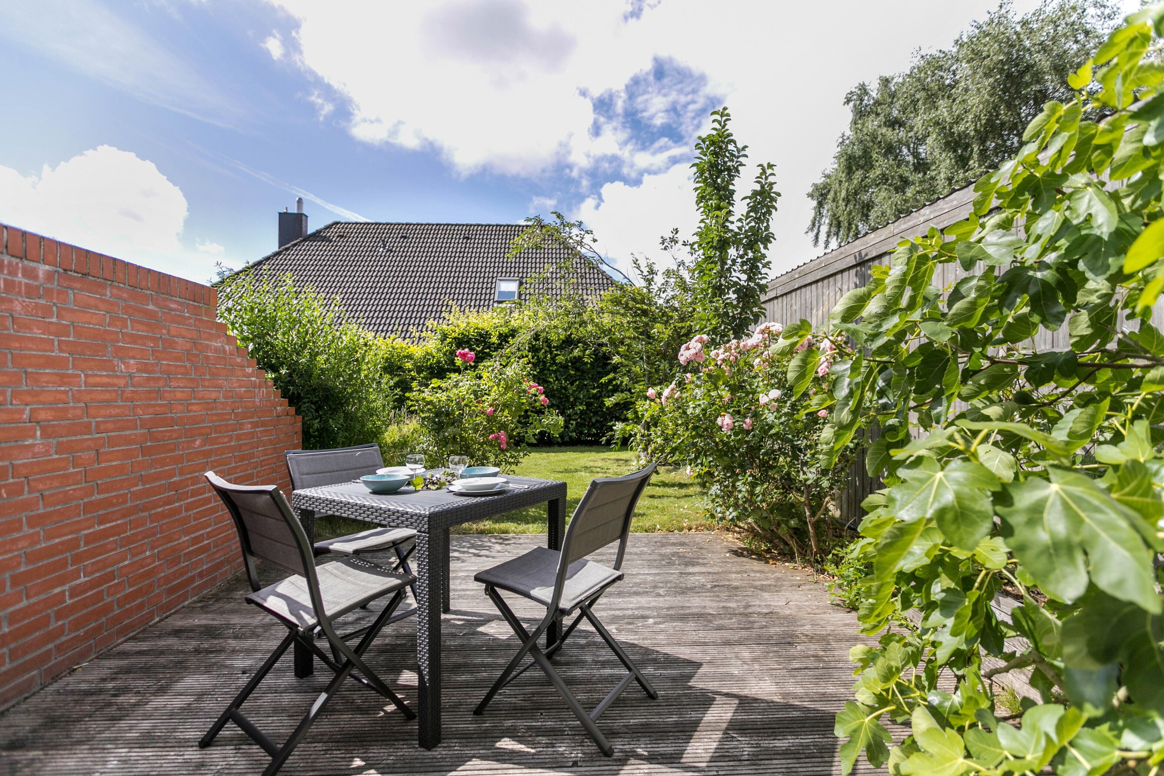 Une terrasse avec une table et des chaises, entourée de verdure et d’un mur de briques.