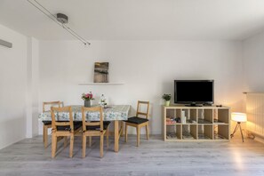 En stue med spisebord, stole, et fladskærms-TV, en reol og en lampe.