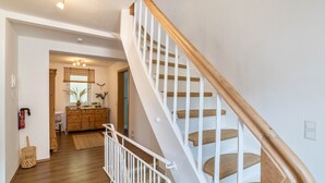 Un escalier avec des rampes en bois et des marches blanches, menant à une pièce dotée d’un plancher en bois et d’un mur blanc.
