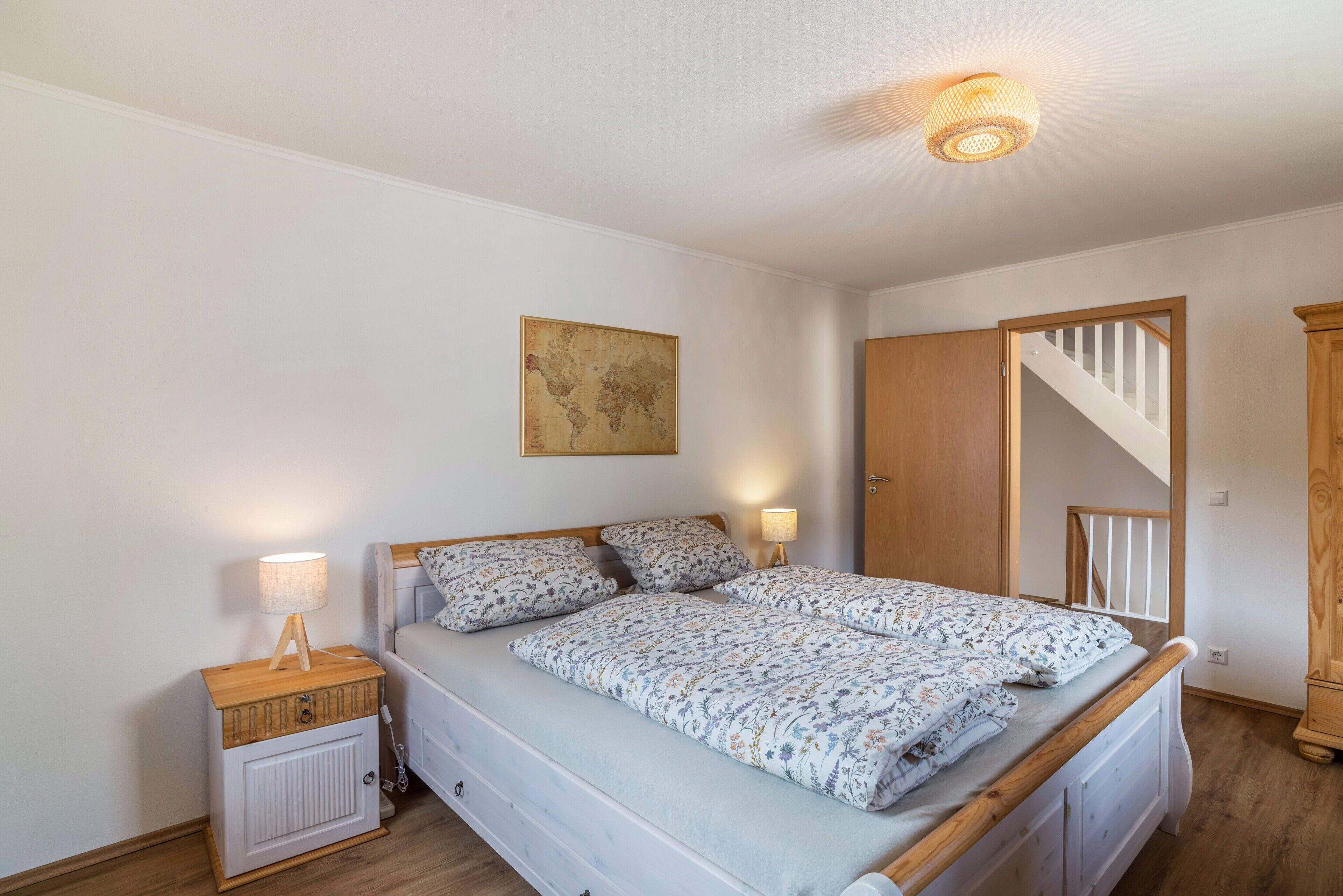 Ein Schlafzimmer mit Bett, Nachttischen, einer Lampe, einer Weltkarte an der Wand und einer Treppe.