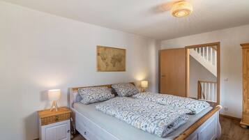 Ein Schlafzimmer mit Bett, Nachttischen, einer Lampe, einer Weltkarte an der Wand und einer Treppe.