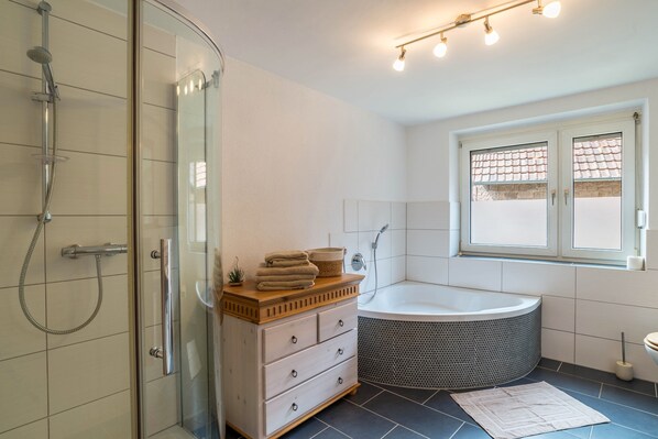 A modern bathroom with a glass shower enclosure, a freestanding bathtub, a wooden vanity with drawers, and a window providing natural light.