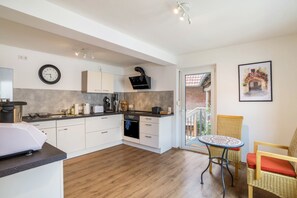 A modern kitchen with white cabinets, a built-in oven, and a dining area with wicker chairs and a small table.