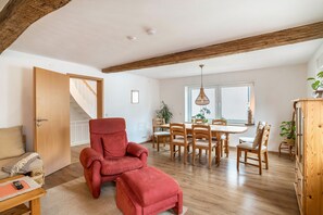 A spacious room with a red armchair, wooden dining table, and a staircase.