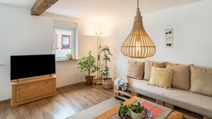 Un salon avec un téléviseur, des meubles en bois, un canapé, un luminaire suspendu et des plantes en pot.