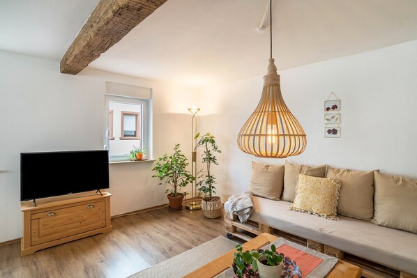 A living room with a TV, wooden furniture, a sofa, a hanging light fixture, and potted plants.