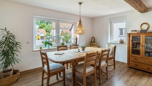 Un espace repas comprenant une table et des chaises en bois, un luminaire suspendu et une fenêtre donnant sur des immeubles.