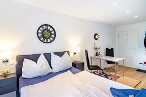 Una habitación de hotel con cama, mesita de noche, lámpara, escritorio, silla y un reloj de pared.