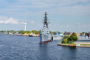 A large naval ship docked at a port with a tower in the background.
