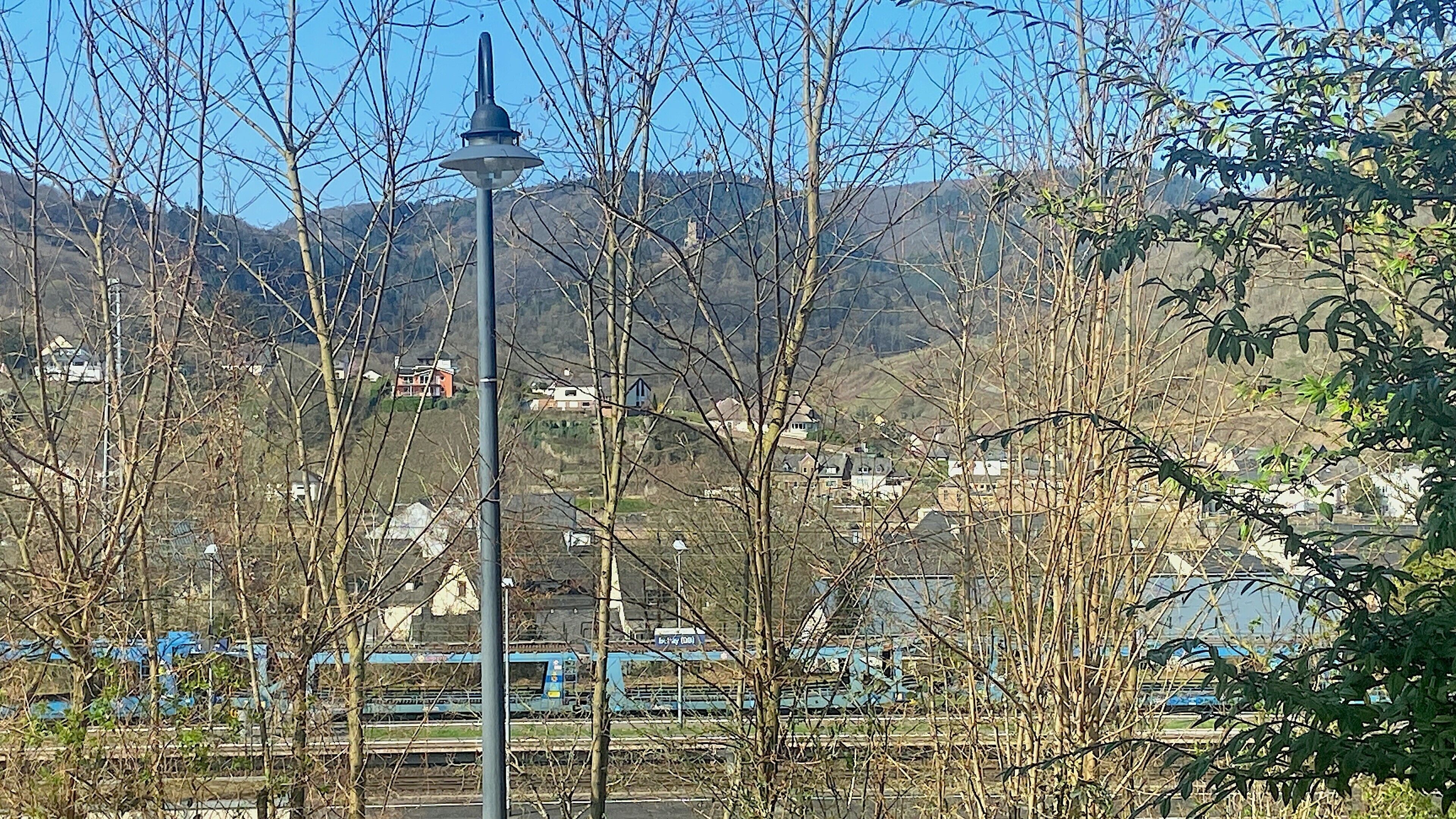 A street lamp, a railway track, and a mountainous landscape with buildings in the background.