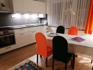 Eine moderne Küche mit weißen Schränken, einem eingebauten Ofen und einer Essecke mit Tisch und Stühlen.