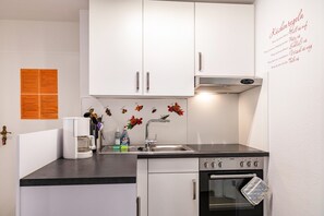 A compact kitchen with white cabinets, a stainless steel sink, a coffee maker, and a small oven.