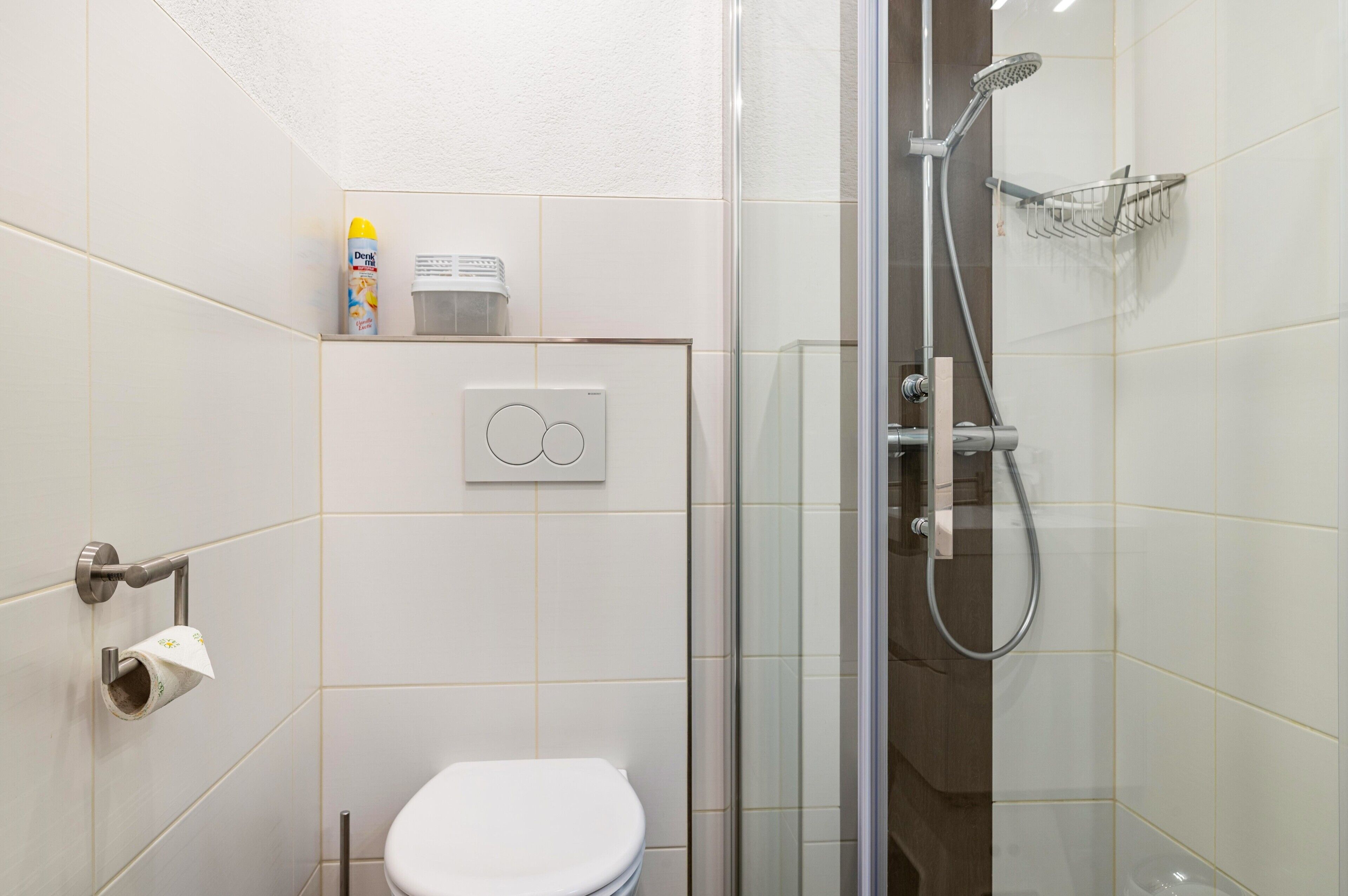 Un bagno con un water, una doccia, un box doccia in vetro, un portasciugamani e un dispenser per sapone.