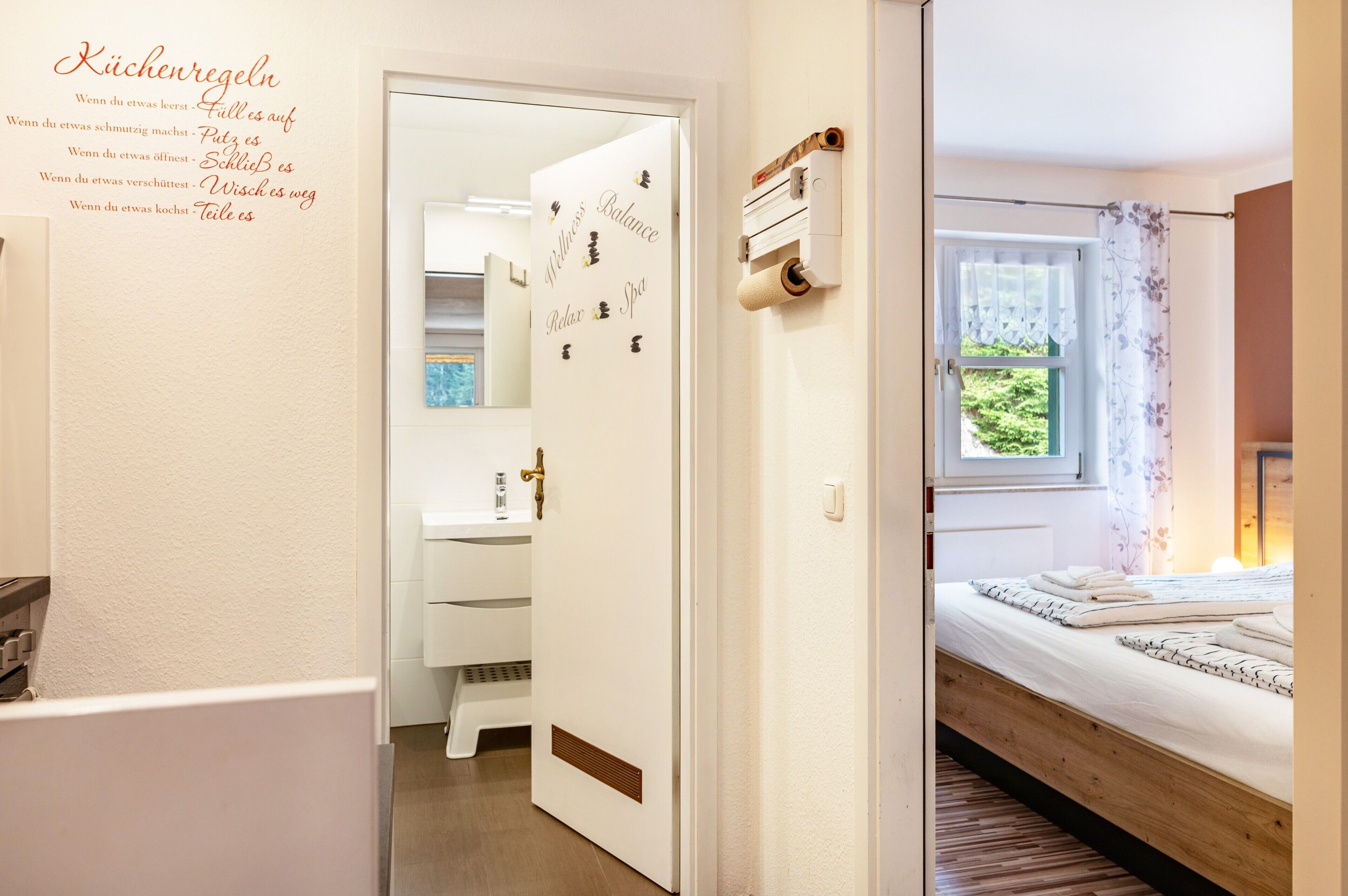 Une chambre d’hôtel avec un lit en bois, une fenêtre avec des rideaux, un distributeur de serviettes fixé au mur et une porte donnant sur une salle de bain.