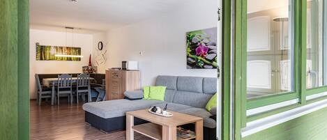 A modern living room with a sofa, a wooden coffee table, and a dining area with chairs and a table.