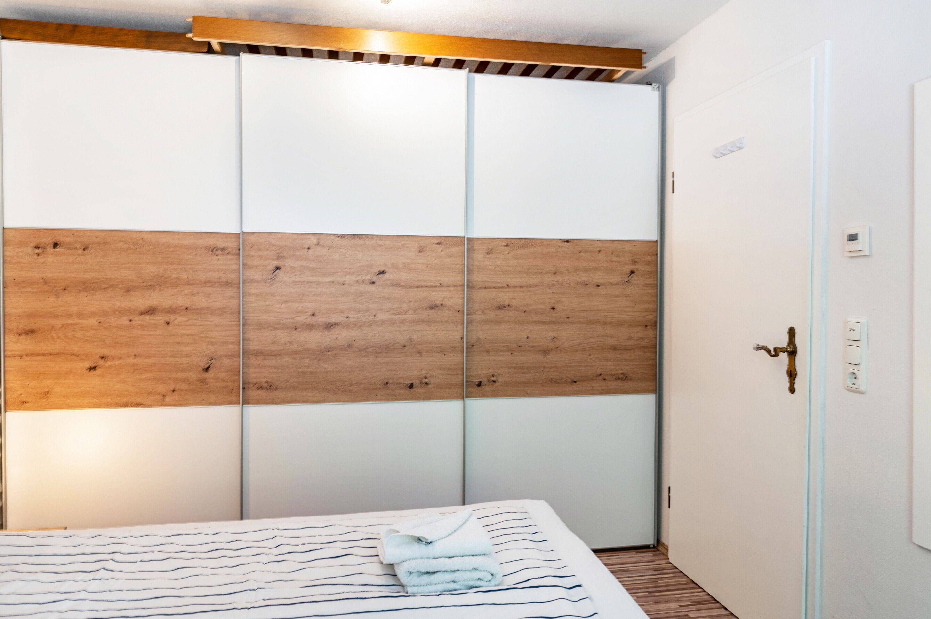 A bedroom with a bed, a wooden panel wall, a white door, and a light switch.