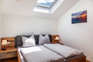 A bedroom with a skylight, a bed with checkered bedding, a headboard, bedside lamps, and a painting on the wall.
