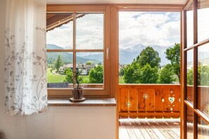 A balcony with a wooden railing, a potted plant, and a view of mountains and greenery.
