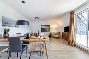 Un salon moderne comprenant un coin repas, un téléviseur à écran plat et de grandes fenêtres avec des rideaux.
