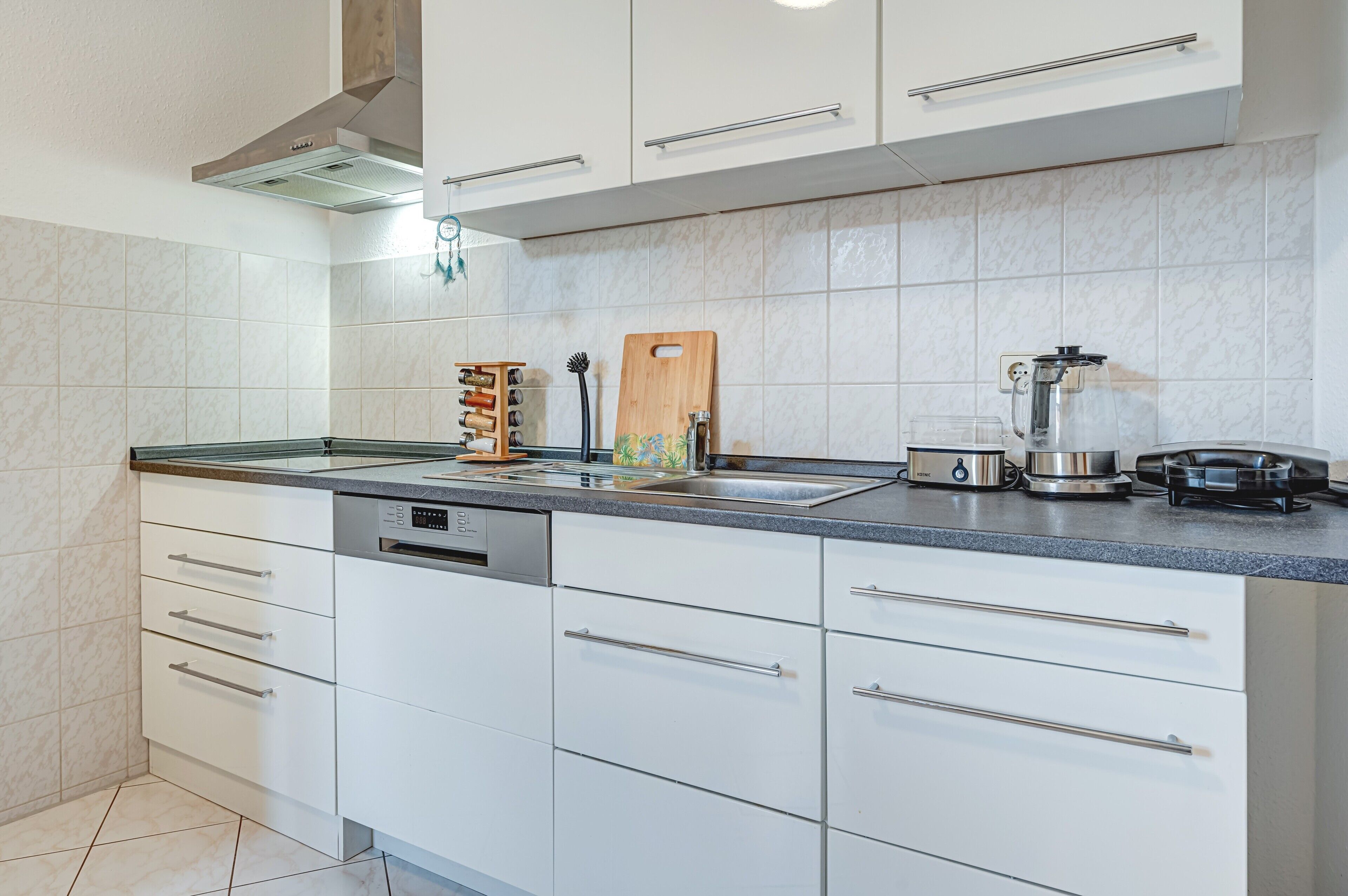 A modern kitchen with white cabinets, a stainless steel range hood, a coffee maker, and a knife block.