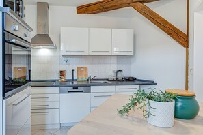A modern kitchen with white cabinets, a wooden ceiling beam, and a countertop with a plant. - Apartment 'Residenz Unter Den Linden Specht' with Wi-Fi (Mühlhausen)