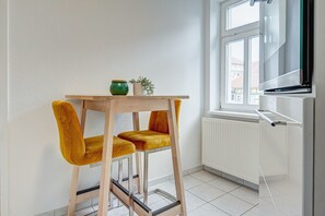 A small room with a wooden table and two yellow chairs, a radiator, and a window with a view of buildings. - Apartment 'Residenz Unter Den Linden Specht' with Wi-Fi (Mühlhausen)