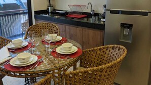 Una cocina moderna con armarios de madera, un refrigerador de acero inoxidable y un comedor con sillas de mimbre y una mesa de vidrio para cuatro.