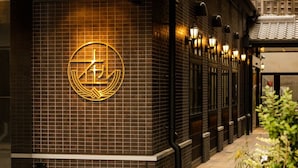 A building facade with a prominent circular logo on a tiled wall, a series of windows, and a traditional tiled roof. - HOTEL ARU KYOTO (Kyoto)