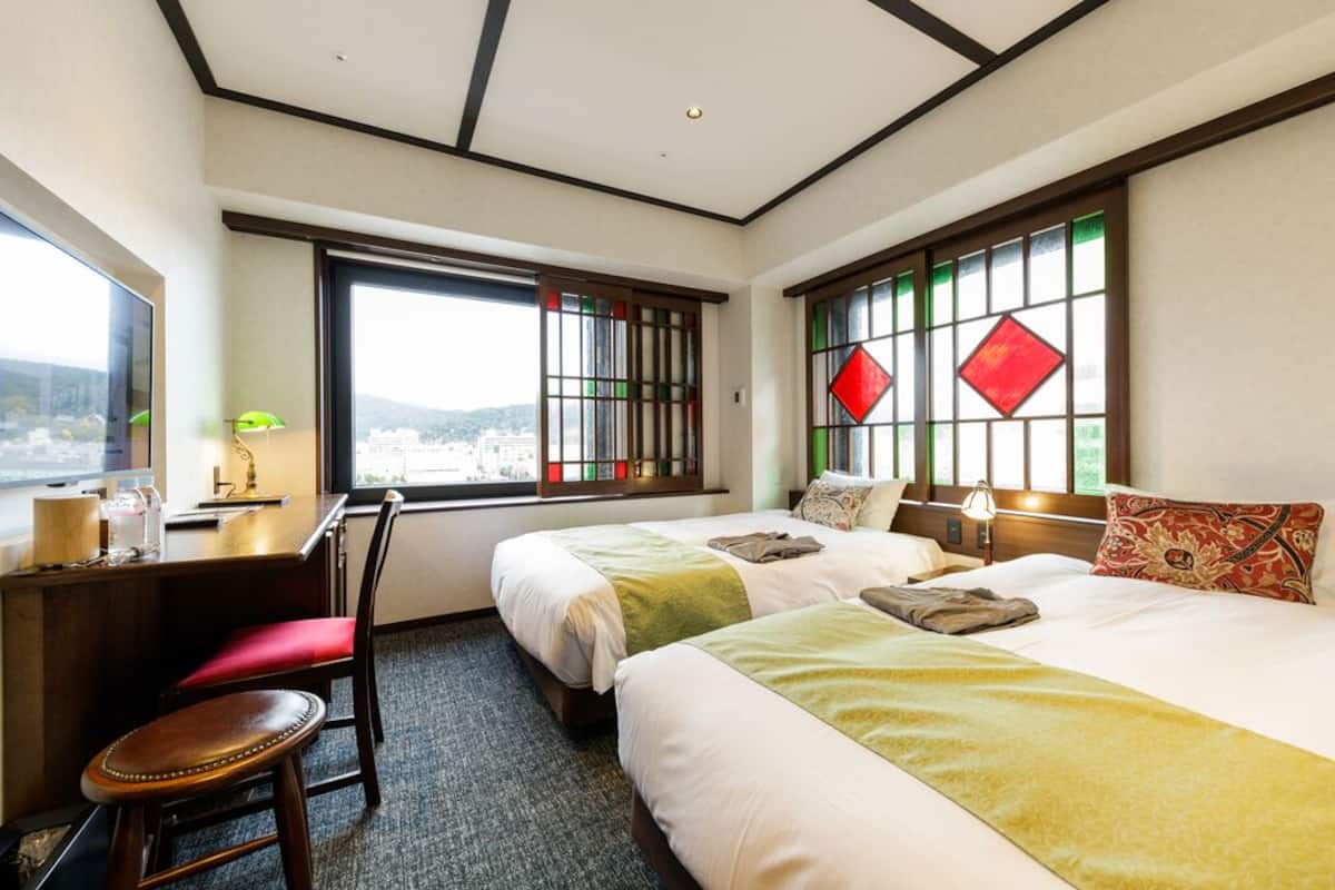 Habitación de hotel con dos camas, un escritorio, una silla y ventana con vistas.